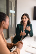 © fizkes - Positive young Latin businesswoman talking to partner at workplace, meeting with consultant for advice, expertise, speaking to colleague, discussing cooperation on project. Vertical shot