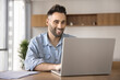 © fizkes - Hispanic man working on laptop sits at table at home office, smiling, reading good news in email, chatting with colleague, solve business-related matters remotely, using new business or hobby platform