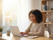 © Eddie Hsieh - Young woman smiling while working on laptop in bright home office.