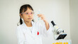 © Thanadon88 - A young girl in a lab coat holding a test tube with a green liquid in it. She is wearing safety goggles and a red shirt