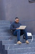 © Wavebreak Media - African American man sitting on concrete steps typing on laptop wearing earbuds beside coffee cup
