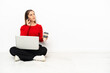 © luismolinero - Young caucasian woman with a laptop sitting on the floor holding coffee to take away and a mobile