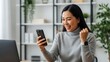 © Ari ortega - Excited Asian Woman Celebrating Success on Smartphone.