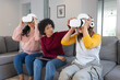 © Wavebreak Media - Diverse female friends sitting on gray sofa in living room using VR headsets holding tablet