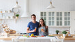 © BestForYou - Man in blue shirt and woman in gray sweater are holding glasses of orange juice and smiling at the camera in kitchen with white brick wall