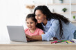 © Prostock-studio - A mother and her daughter sit together at a table, engaged in an enjoyable learning activity on a laptop. They share smiles and laughter, creating a joyful atmosphere.