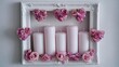 © id - Five pale pillar candles arranged within an ornate white picture frame adorned with pink floral decorations