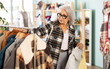 © JackF - Elderly woman stands near the rail with outerwear, she looks at the assortment of down jackets before buying. Pensioner buys a warm jacket in a store of clothes