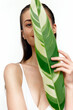 © VICHIZH - Young model holding a large green leaf, showcasing natural beauty and elegance with a serene expression, ideal for wellness and eco-friendly concepts.