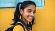 © Oleh - Young indian woman wearing a backpack and yellow shirt, carrying a positive attitude and smiling brightly at the viewer against a vibrant yellow and blue background