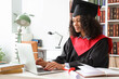 © Pixel-Shot - Pretty African-American female graduate with laptop sitting at table in library