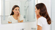© ArtFocus Studio - Young woman examining her face with acne in the bathroom mirror, touching her cheek with concern in a bright, minimalist setting.