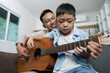 © itchaznong - Father teaching son to play guitar at home