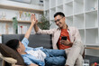 © itchaznong - Father and son sharing a high-five in a cozy living room