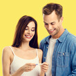 © vgstudio - Love, relationship, new parents, happy family concept - joyful young attractive couple, husband, wife finding out results of pregnancy test, isolated vivid yellow color background. Square image