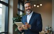 © li - Happy middle aged business man. Ceo wearing suit standing in office. Man using digital tablet. High quality