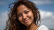 © Thares2020 - A happy young woman with curly brown hair and tanned skin smiles outdoors under a sunny blue sky