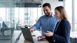 © Николай Срибяник - Diverse male and female colleagues collaborating on a project using a laptop in a modern corporate office, smiling and discussing.