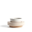 © Samina - Minimalist ceramic bowl resting on stacked natural wood and beige stone serving pedestal isolated on white