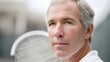 © pkproject - Close up portrait of a contemplative senior male tennis player with gray hair set against an outdoor court background with a blurred racket