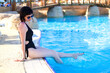 © ALEXEY - middle aged woman sits on the edge of a pool with her feet in the water.