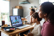 © Marko Geber - Adult mother with child sons on concerned telehealth call in kitchen