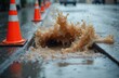 © Pete - Street flood with dirty sewage water flowing from manhole. Orange cones set on street with flooded road after rain. Urban flooding causes overflow pollution. Road drainage malfunction creates