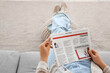 © Pixel-Shot - Young woman with newspaper sitting on sofa at home, top view