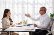 © David - Business senior man and asian woman discussing documents in bright office, smiling and engaged in friendly conversation during business meeting