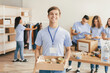 © Prostock-studio - A group of volunteers works together at a community center, packing donations into boxes. One volunteer smiles while holding a box of goods, while others organize supplies and take notes.