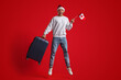 © Prostock-studio - A young man is joyfully jumping in the air, holding a small Canadian flag and a suitcase. He wears a festive hat and smiles widely, celebrating the holiday spirit.
