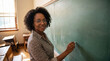 © Eduardo Accorinti - Portrait of smiling african american teacher looking at camera while writing on empty chalkboard in a vintage classroom
