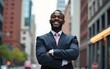 © gu - Business man standing with arms crossed, looking confident and proud in the city alone. Portrait of a black male entrepreneur or worker showing vision, ambition and success with arms folded downtown