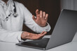 © ImageFlow - Doctor consulting online through laptop using hand gestures, symbolizing future teleconsultation and AI healthcare system concept on dark background.