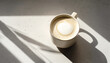 © Victoria - coffee latte mug sitting on a textured table illuminated by natural morning sunlight creating strong diagonal shadows for a minimalist and relaxing atmosphere