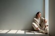© Anna Lurye - Woman sitting on the floor by a window, leaning against the wall, dressed in soft neutral tones, reflecting on feelings of depression and solitude in a serene atmosphere