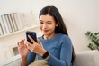 © Hip.hub - Woman smiling while using smartphone at home in a cozy living room during the day
