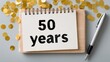 © Emilio - Notebook with handwritten 50 years on wooden board with gold confetti and pen. 50th anniversary planning concept, milestone celebration, festive flat lay