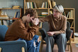 © Mediaphotos - Teenager sitting with head in hands being comforted by adult woman during group therapy session with bookshelves in background