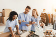 © Prostock-studio - Three volunteers work together in a community service center, sorting food donations and preparing boxes. They display teamwork while coordinating items and writing notes for the distribution.