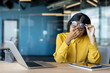 © Tetiana - Tired and overwhelmed young Indian businesswoman sitting at her office desk. holding her glasses and rubbing her eyes with her hand