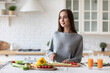 © BestForYou - Woman in a gray sweater is standing in a kitchen with fresh vegetables