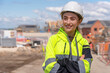© Iryna - Portrait of smiling young woman builder in bright safety gear and hard hat with arms crossed  at construction site
