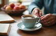 © Viktor - Elderly woman hands stir coffee in a light blue cup on a wooden table. An open book and a bowl of apples are nearby. Relaxing morning moment.