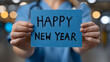 © Daniel - A nurse holding a blue paper and HAPPY NEW YEAR written on it. Celebrate the new year with nurses. Happy New Year for health care, wellness, and creative medical concepts. Generative AI