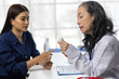 © Wasan - Senior female doctor holding a medicine bottle, explaining medication and giving advice to patient during a medical consultation in hospital.