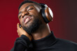 © SHOTPRIME STUDIO - A young Black man enjoying music with headphones on, exuding relaxation and joy, set against a rich red background