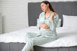 © Pixel-Shot - Pregnant young woman in pajamas suffering from pain in shoulder on bed at home