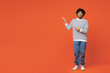 © ViDi Studio - Full body young smiling happy Indian man he wear striped sweatshirt casual clothes point index finger aside on area mock up isolated on plain red orange background studio portrait. Lifestyle concept.