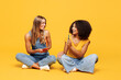 © ViDi Studio - Full body two young happy friends buddies women wear denim casual clothes sit together hold in hand use mobile cell phone isolated on plain yellow orange background studio portrait. Lifestyle concept.
